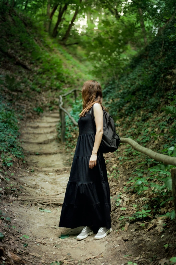 Woman in black dress walks on forest path